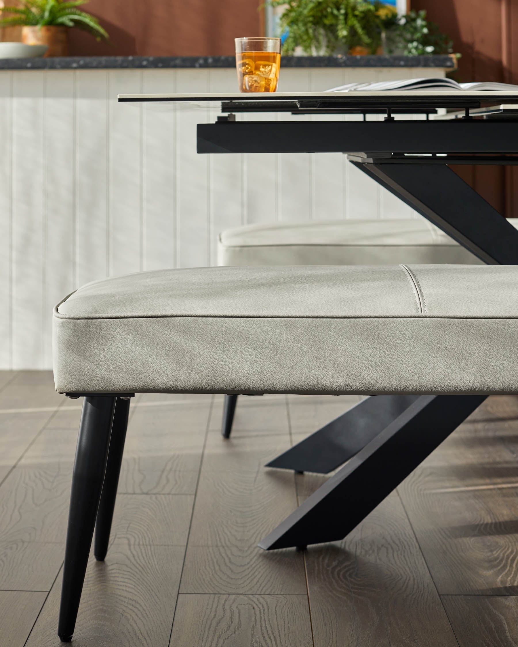 Banquette 3 places sans dossier en similicuir gris clair.