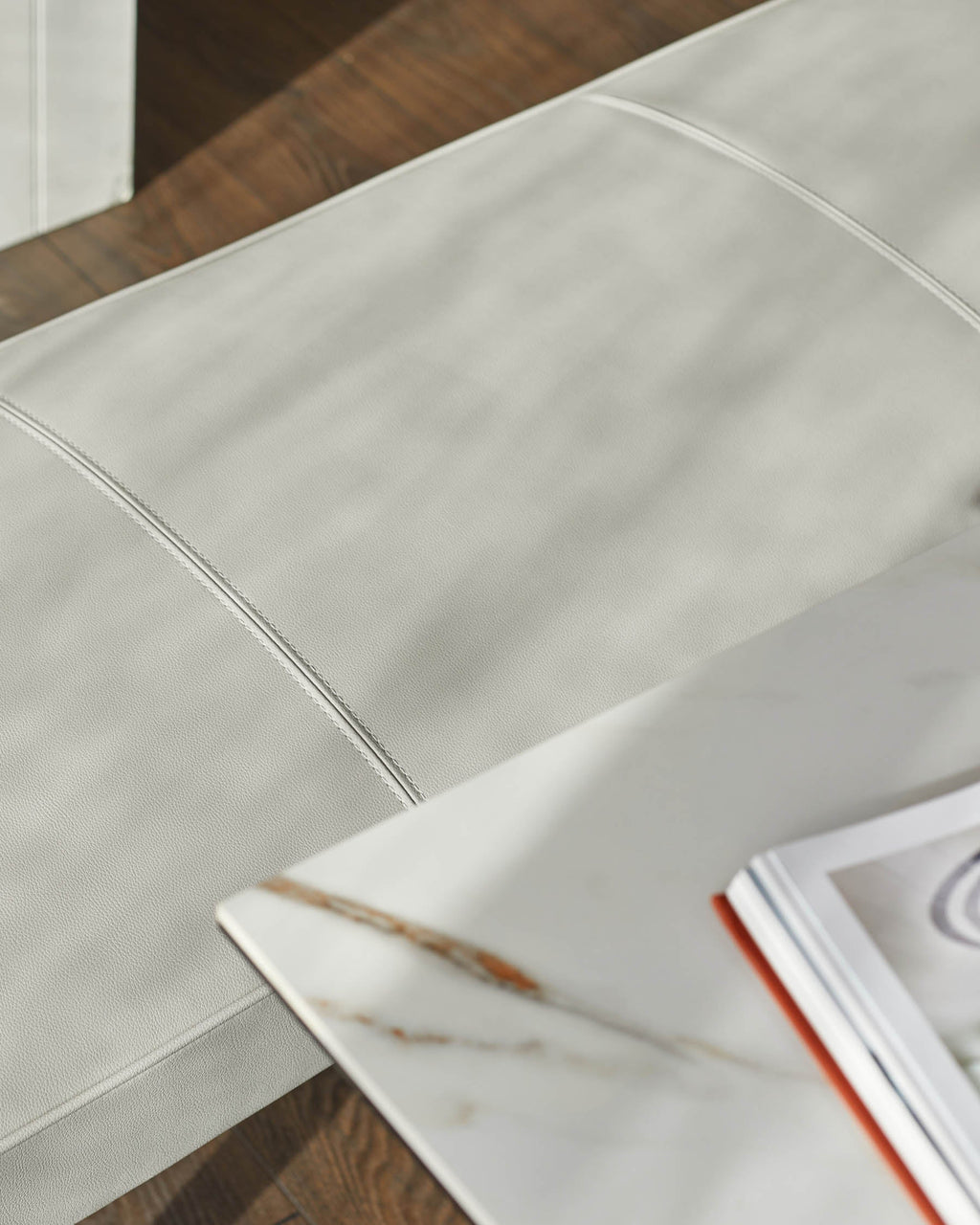 Banquette 3 places sans dossier en similicuir gris clair.