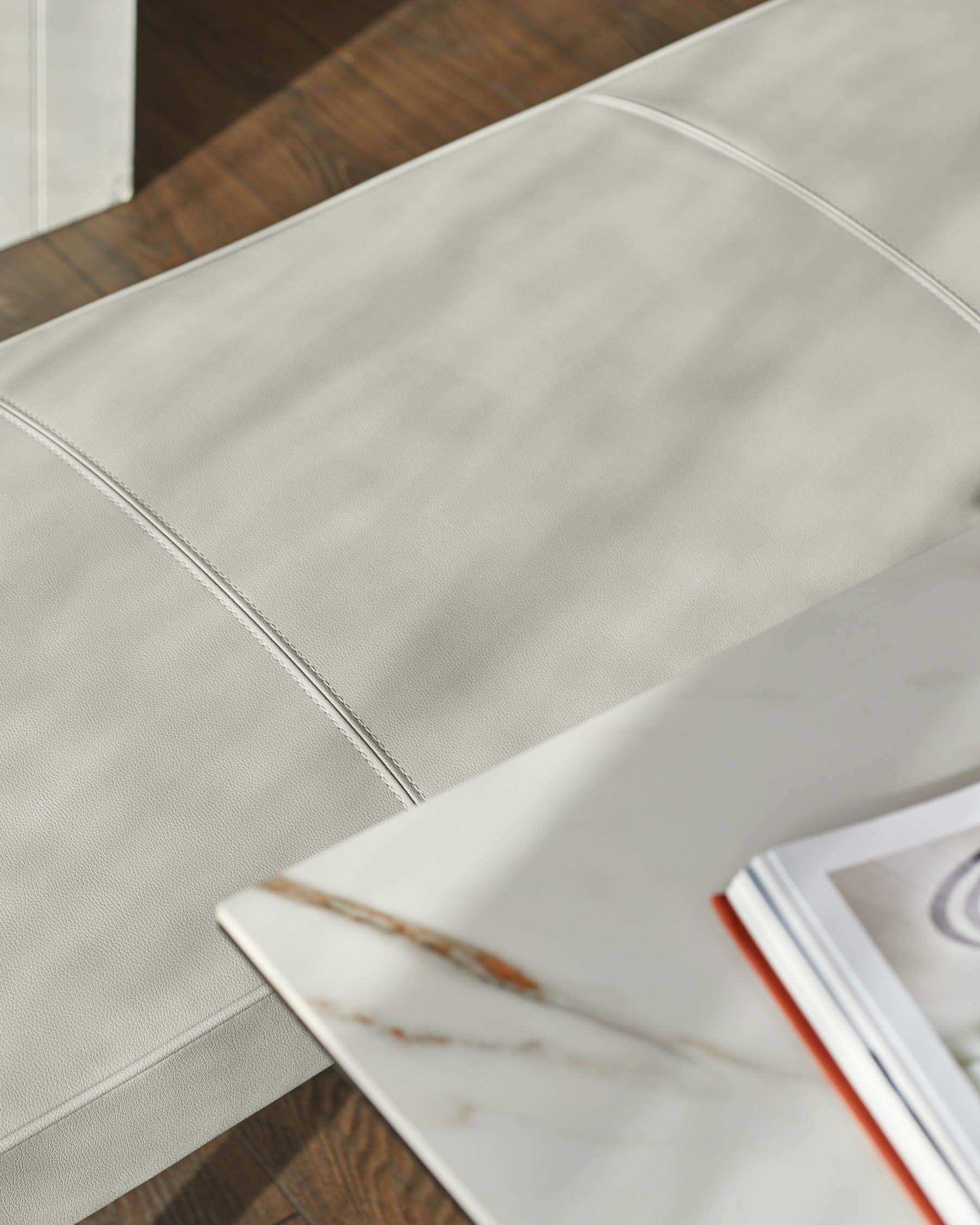 Banquette 3 places sans dossier en similicuir gris clair.