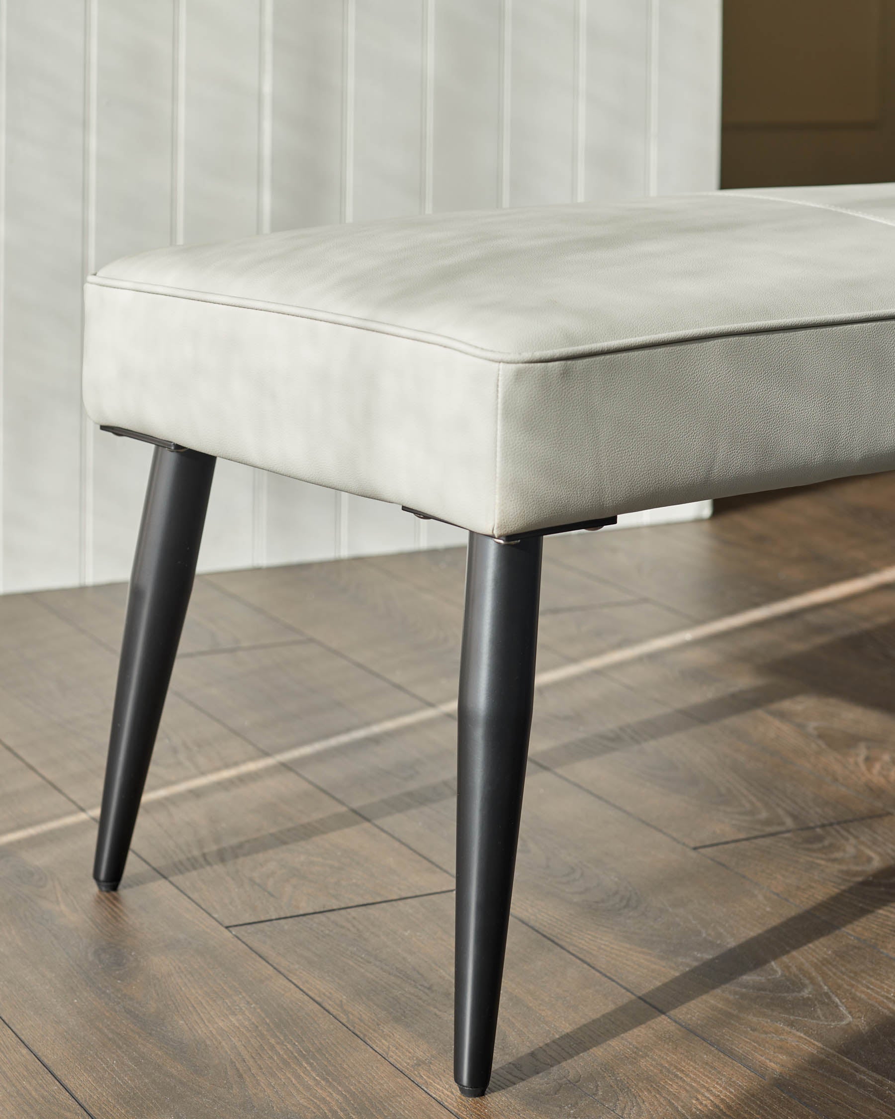 Banquette 3 places sans dossier en similicuir gris clair.